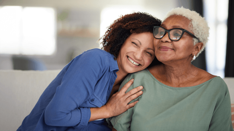 An adult woman and an elderly woman sitting close together and smiling