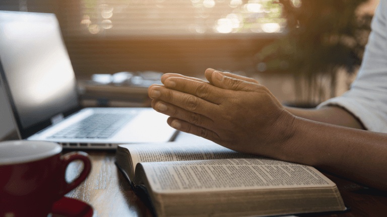 Person praying over an open Bible at a desk